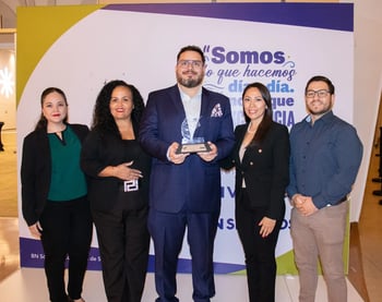 Grupo de cinco personas en un evento, un hombre al centro sosteniendo un trofeo con logotipos de BN y CICR, acompañados por dos mujeres a cada lado.
