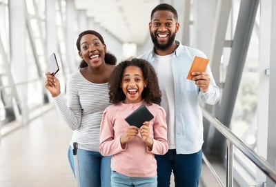 Familia sonriente en aeropuerto sosteniendo pasaportes, lista para abordar un viaje.