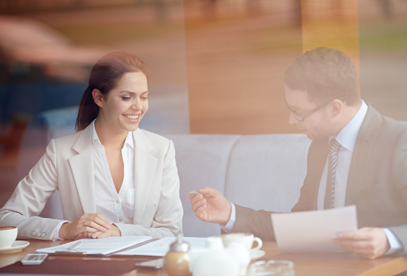 Reunión de negocios entre un hombre y una mujer en una cafetería, conversando y revisando documentos.