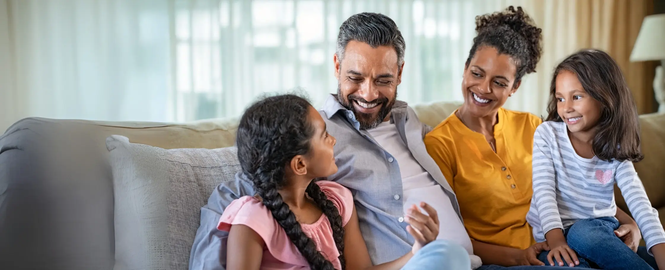 Familia sonriente sentada en el sofá conversando y compartiendo en casa