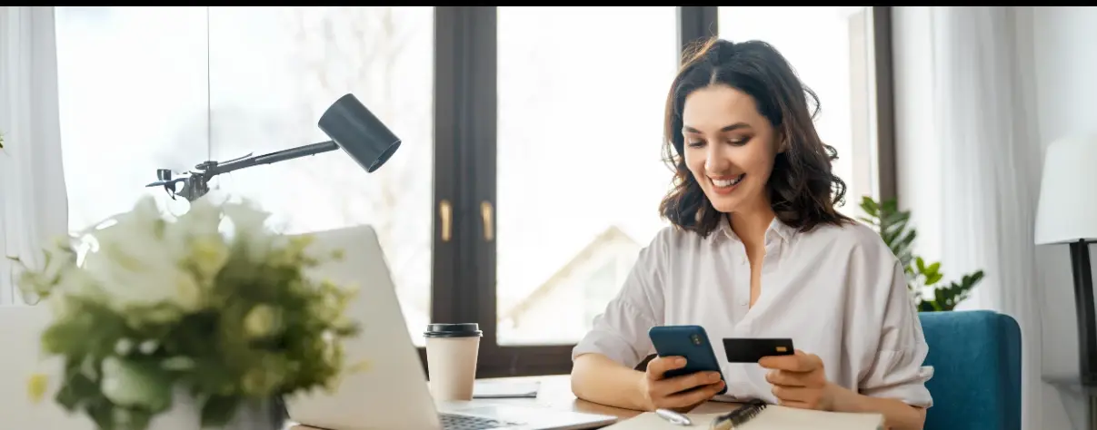 Mujer sonriendo mientras realiza una compra en línea con su tarjeta y teléfono móvil