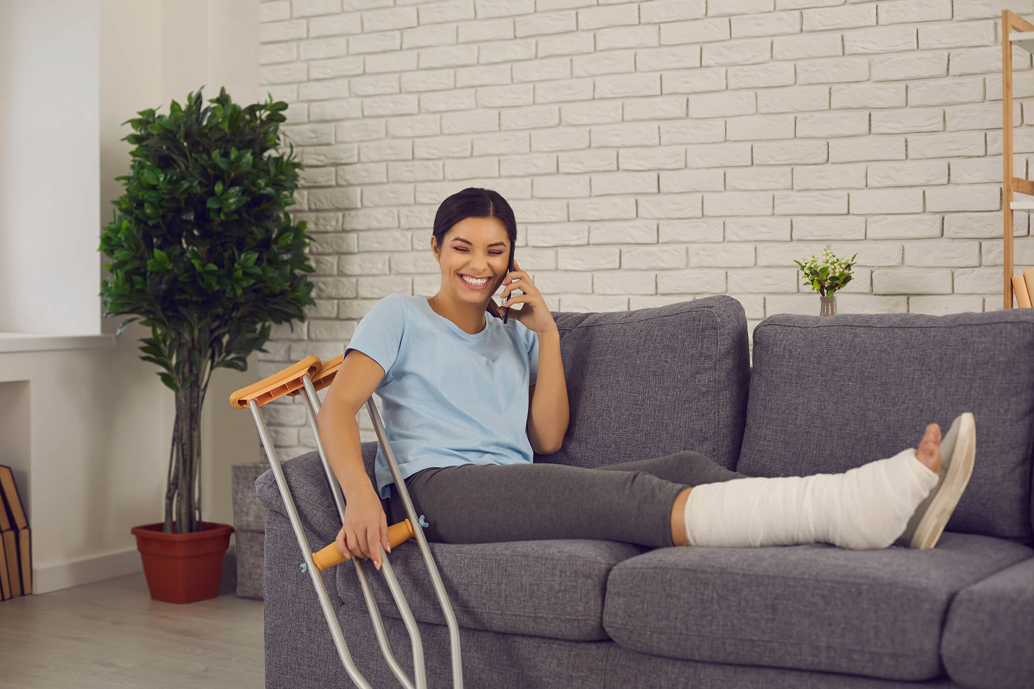 Mujer con muletas y pierna enyesada sentada en un sofá mientras habla por teléfono.