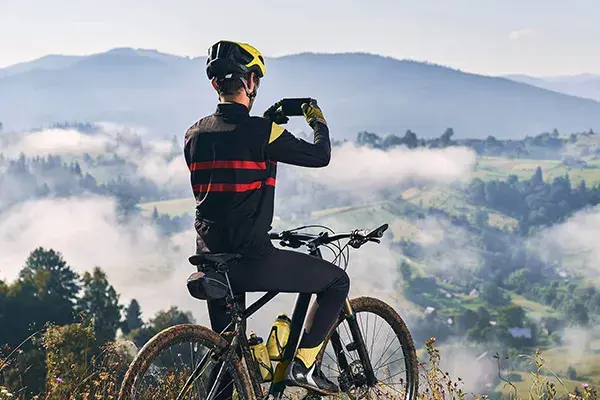 Ciclista con casco y ropa deportiva tomando foto de paisaje montañoso con neblina.