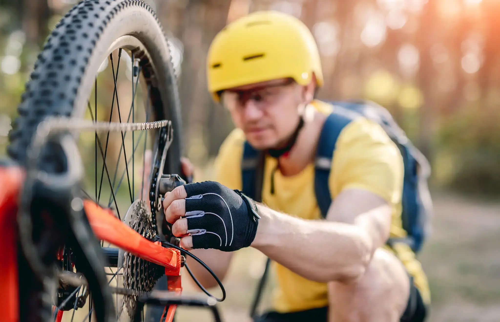 Ciclista con casco amarillo revisando el mecanismo de la rueda trasera de su bicicleta en un entorno al aire libre.