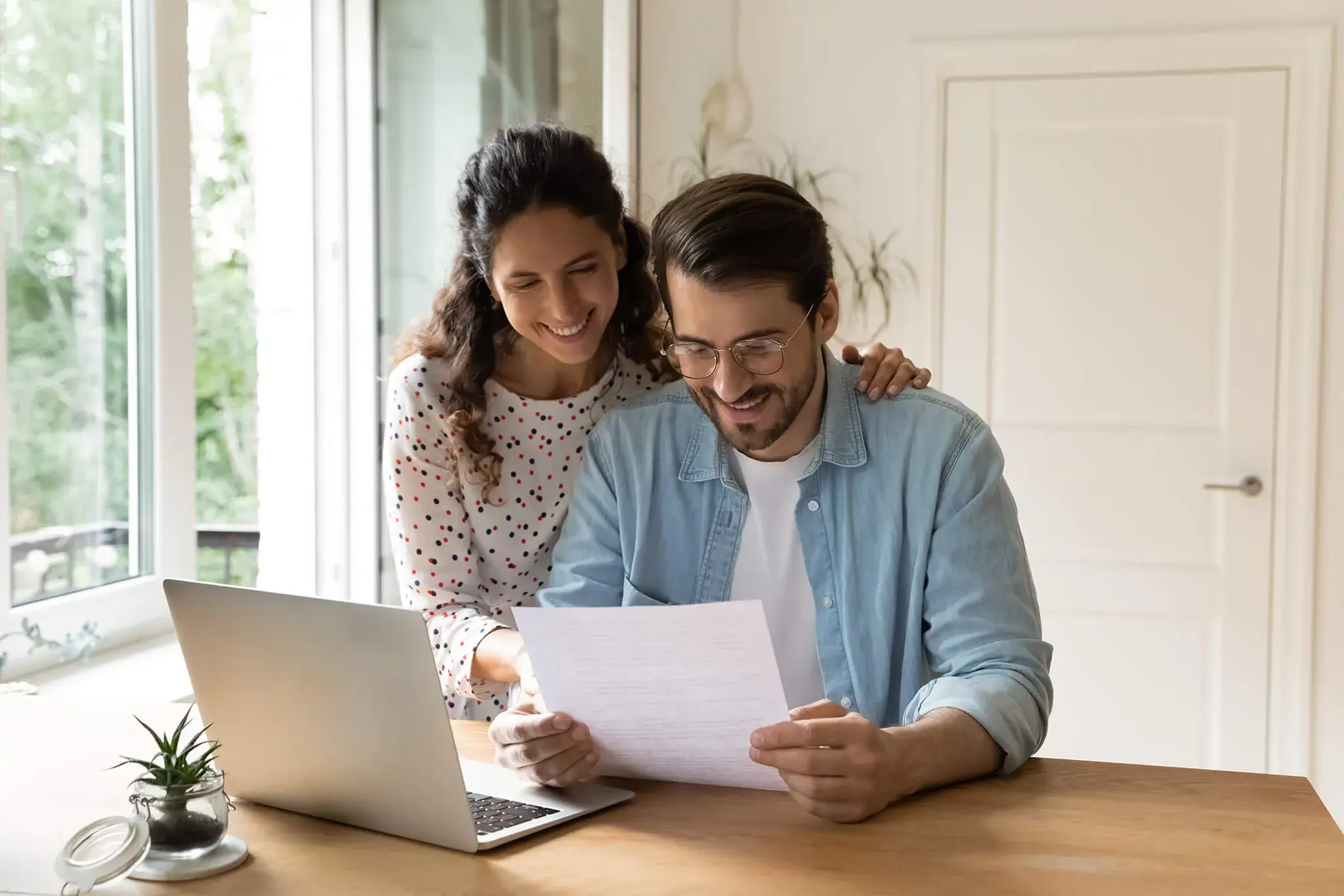 Pareja revisando un documento juntos frente a una laptop en casa.
