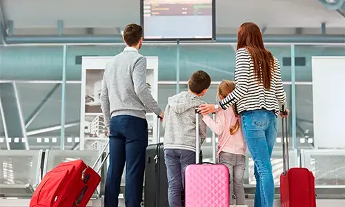 Familia con maletas observando la pantalla de vuelos en un aeropuerto.