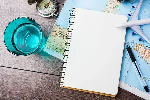 Vaso con agua, libreta, bolígrafo y mapa sobre mesa de madera.