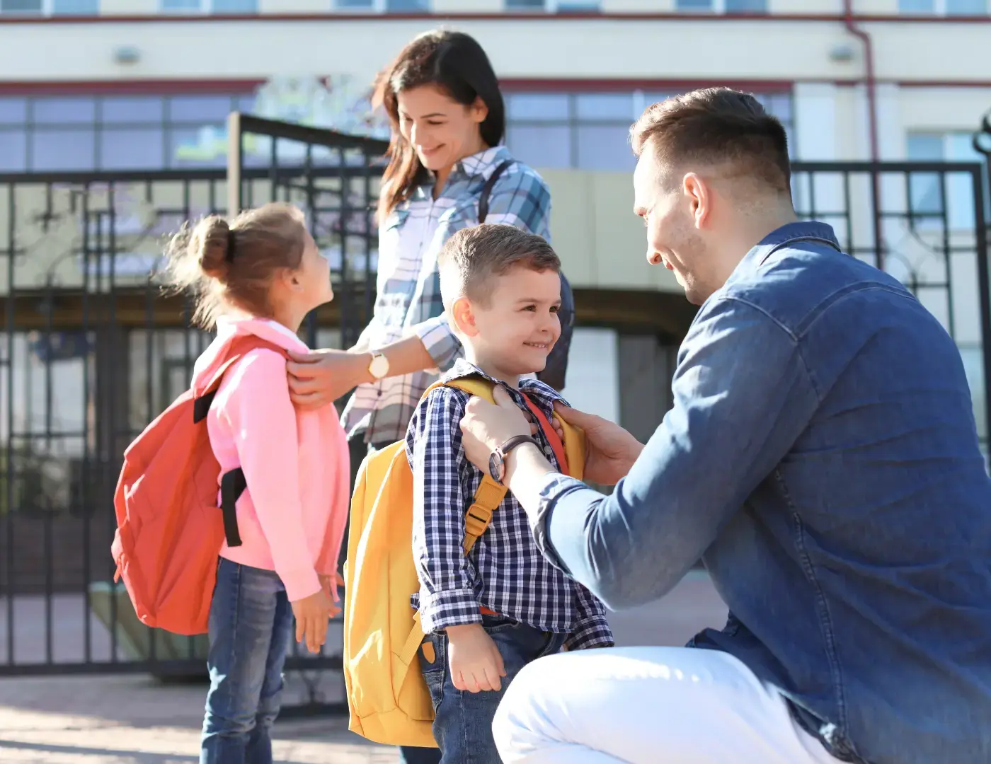 Padres acompañando a sus hijos a la escuela y ajustando sus mochilas en la entrada.
