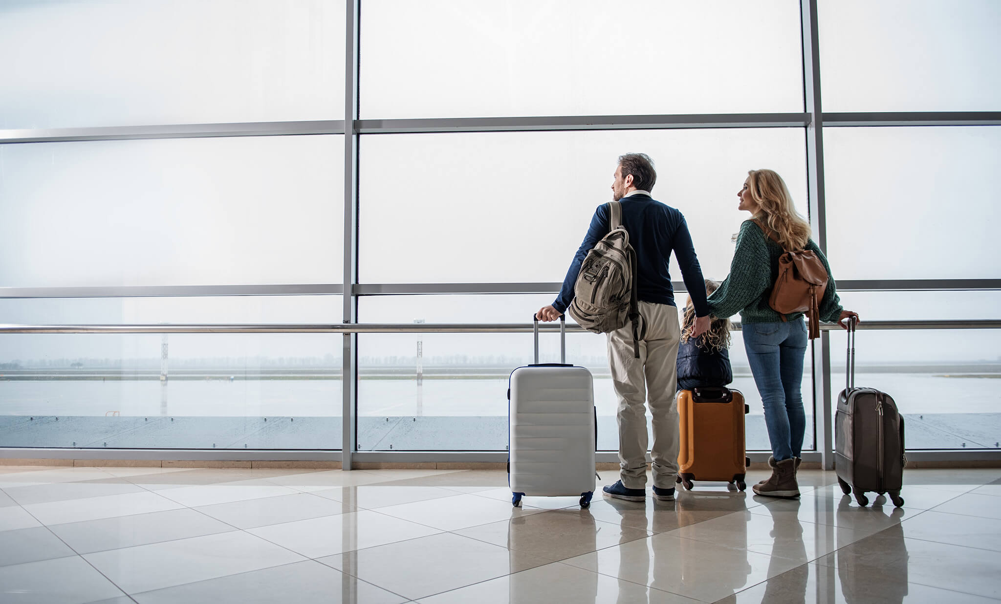 Pareja en un aeropuerto observando la pista con maletas de viaje.