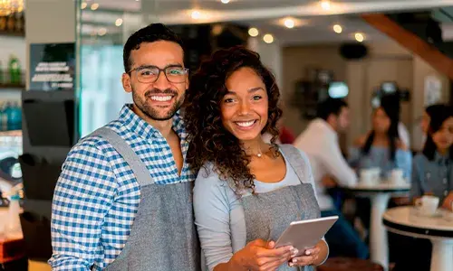 Pareja de emprendedores con uniforme en su negocio sonriendo a cámara.