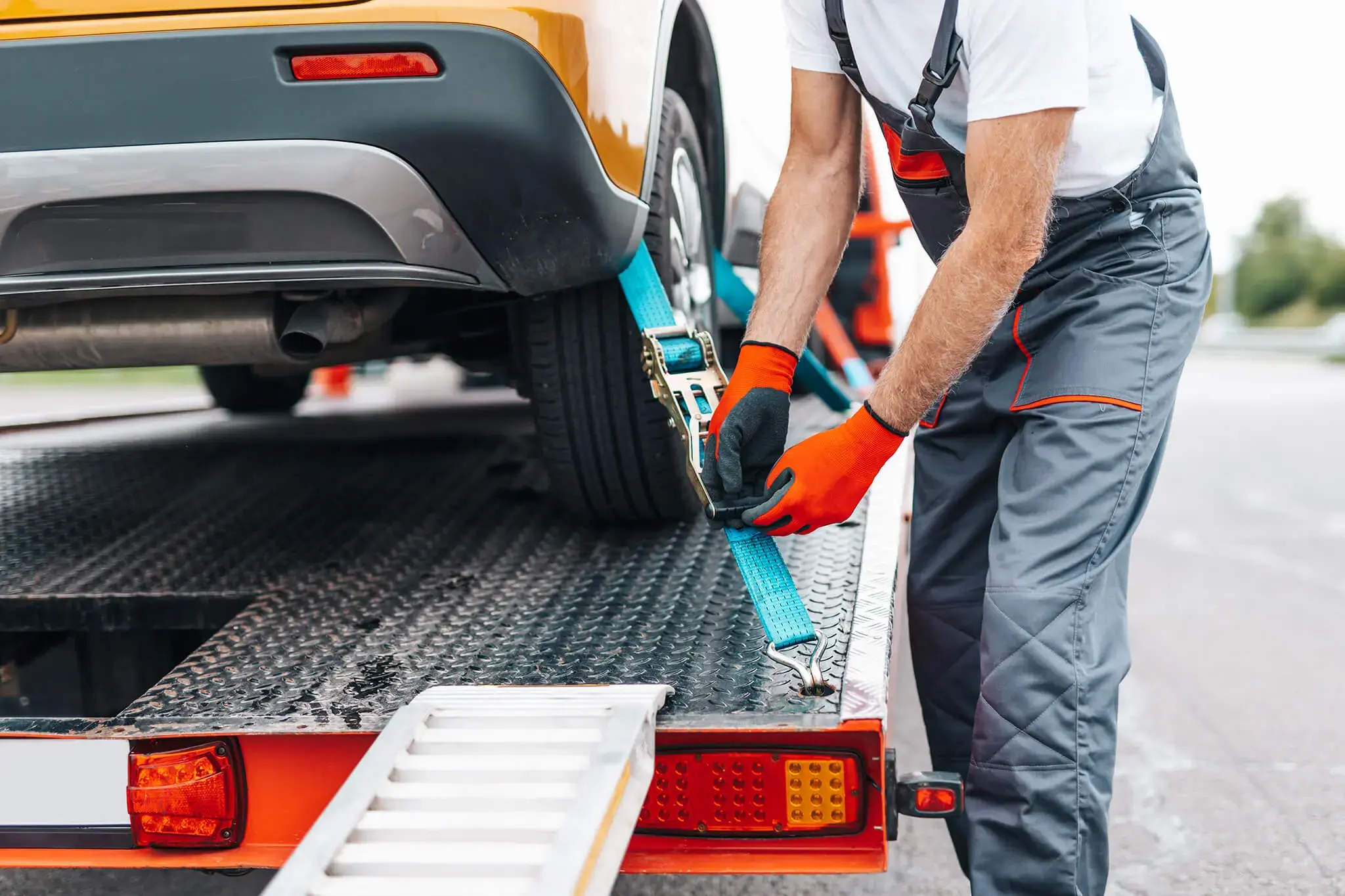 Trabajador asegurando un automóvil con una correa en la plataforma de una grúa de remolque.