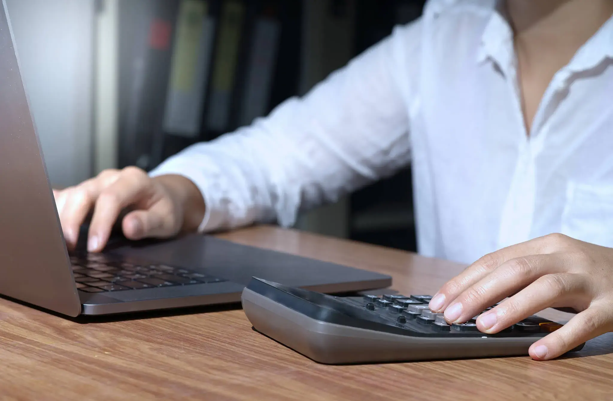 Persona usando una laptop y una calculadora sobre un escritorio de madera.