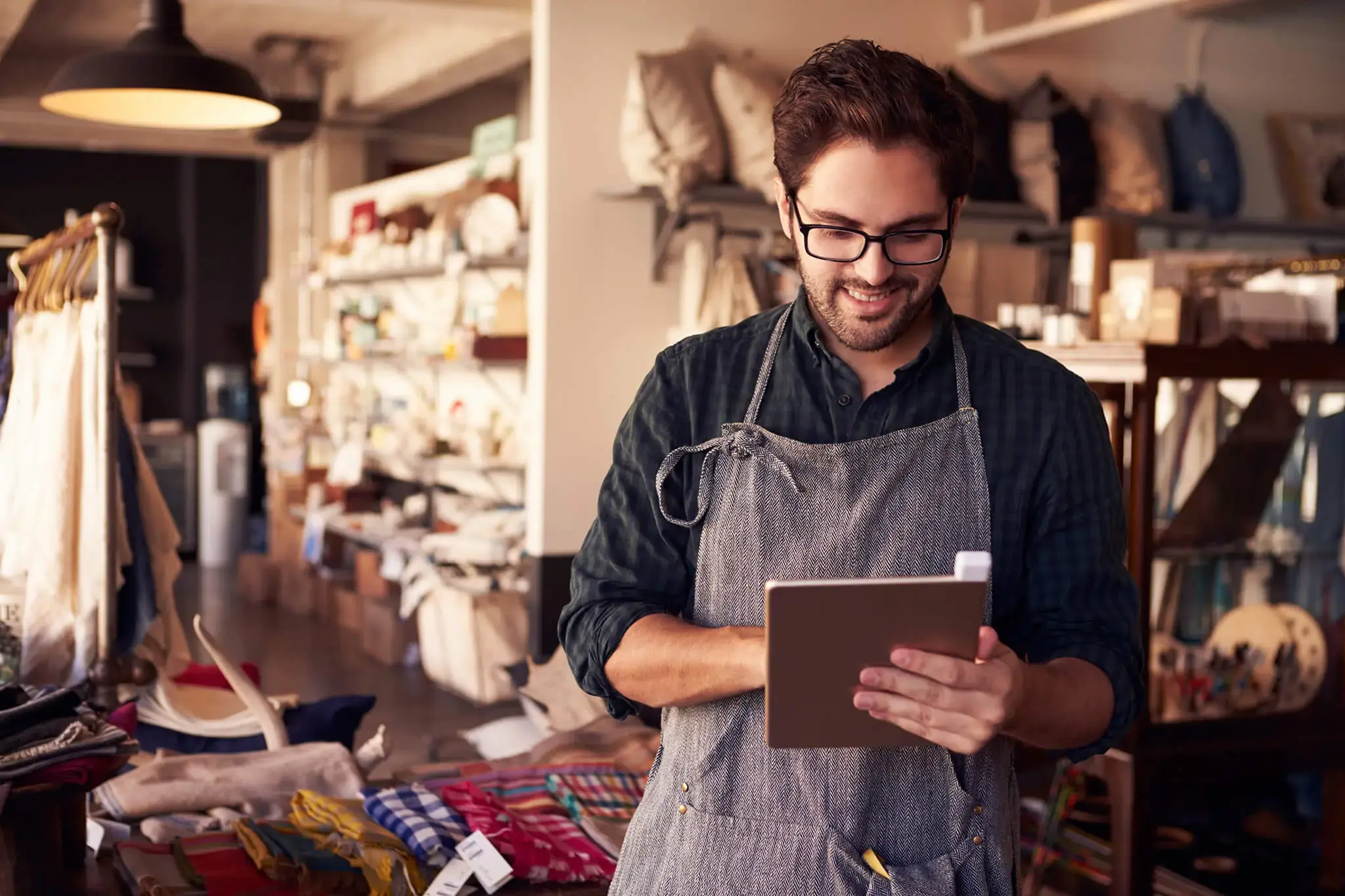 Hombre con delantal trabajando en una tienda, usando una tableta digital para gestionar inventario o ventas.