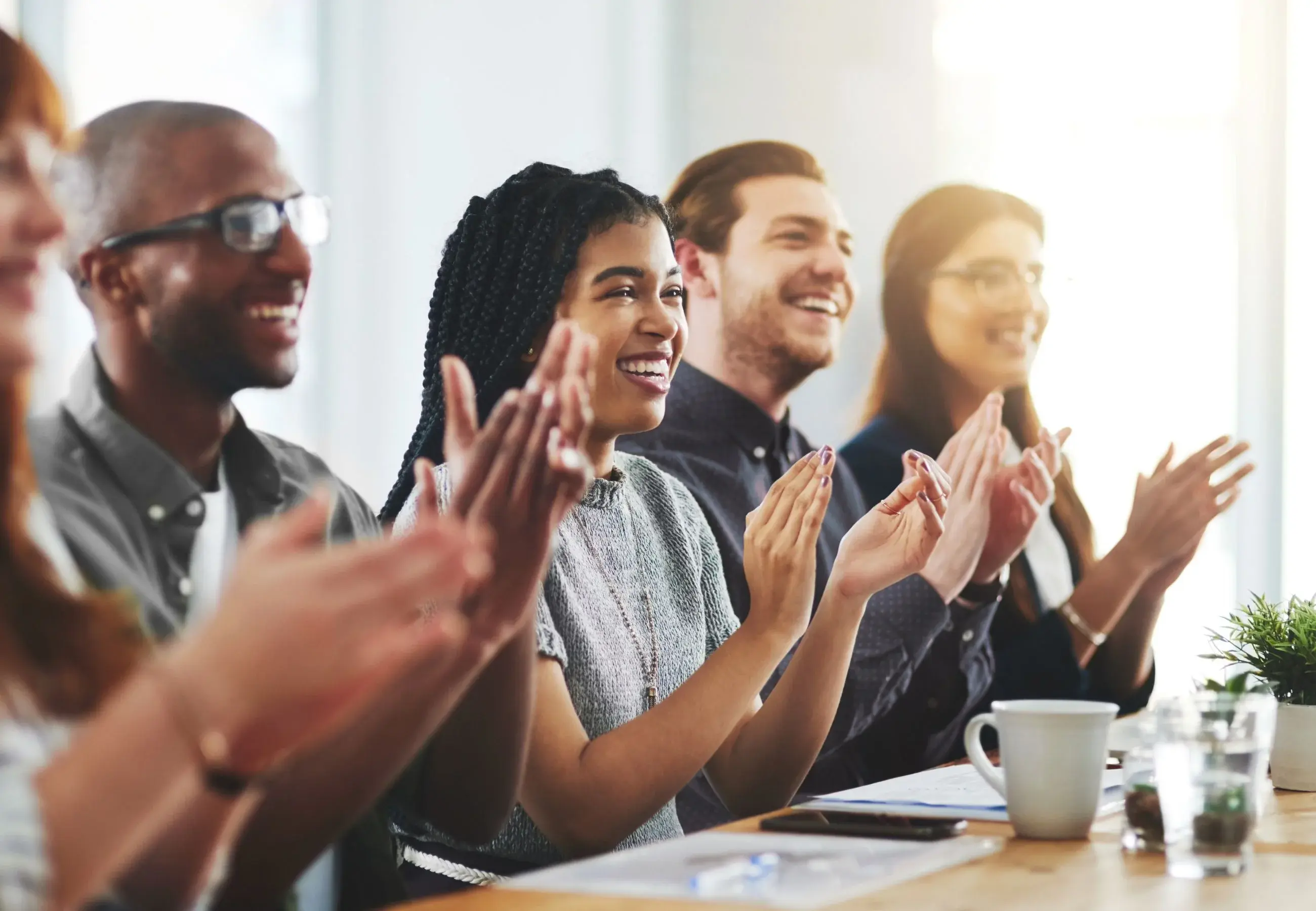 Grupo diverso de personas sonriendo y aplaudiendo en reunión.