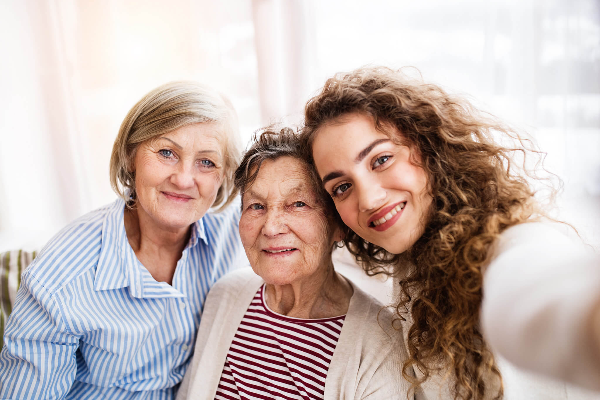 Tres mujeres de distintas generaciones sonriendo mientras posan para una selfie en un interior iluminado.